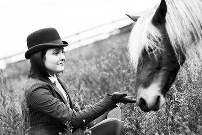 Smiling woman sitting by pony on field