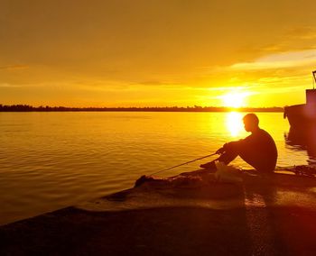 Silhouette man fishing in sea against sky during sunset