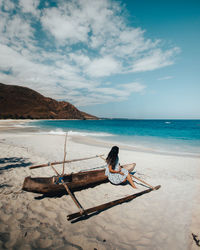 Full length of woman sitting on beach against sky