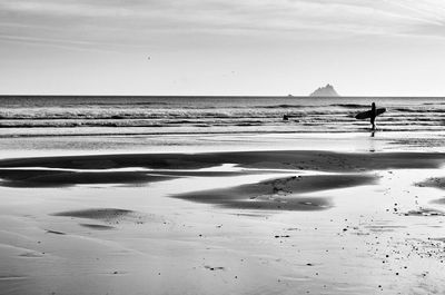 Silhouette man with surfboard at beach against sky