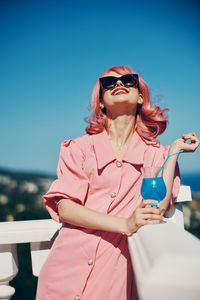 Young woman wearing sunglasses while standing against blue sky