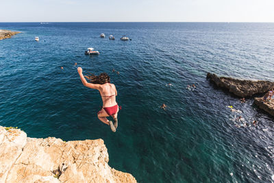 Woman jumping on rock in sea against sky