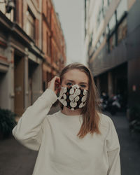 Portrait of beautiful woman wearing mask standing on street in city