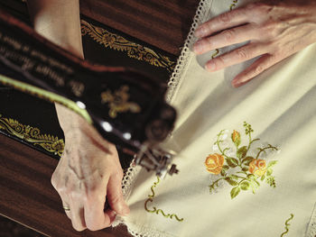 Senior lady in glasses using retro sewing machine to create linen napkin in cozy room at home