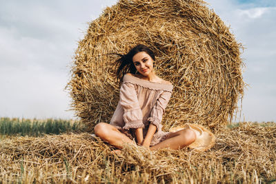 Smiling woman in sunglasses with bare shoulders on a background of wheat field and bales of hay.