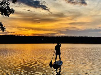 Silhouette man in lake against sky during sunset