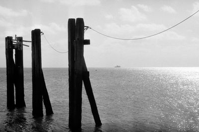 Wooden posts in sea against sky