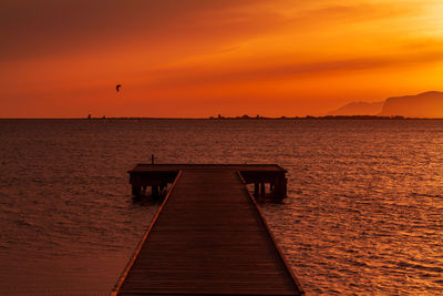 Wooden pier over sea against orange sky