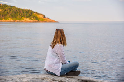 Woman sitting by sea against sky