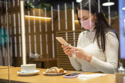 Young woman using mobile phone while sitting at restaurant