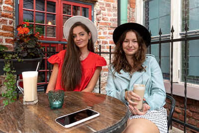 Two cheerful pretty young women drinking coffee, talking and laughing in outdoor cafe