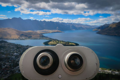 Close-up of coin-operated binoculars by queenstown gondola overlooking lake wakatipu against sky