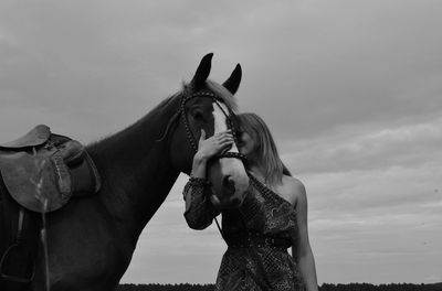 Woman embracing horse while standing against sky