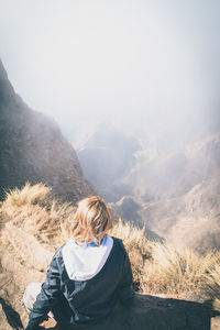 Rear view of woman sitting on mountain peak