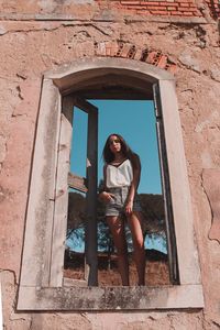 Portrait of young woman standing against window of building