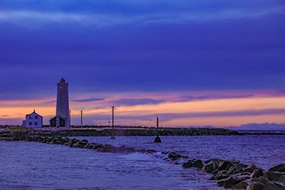 Lighthouse by sea against sky during sunset