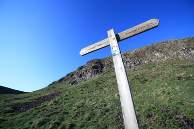 Low angle view of road sign on hill against clear blue sky