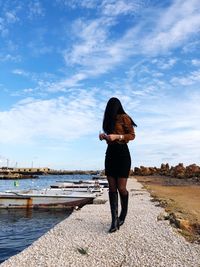 Young woman standing at shore against cloudy sky