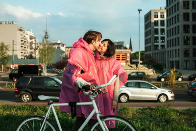 Young couple wearing pink raincoat while kissing in city