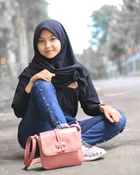 Portrait of young woman sitting on street in city