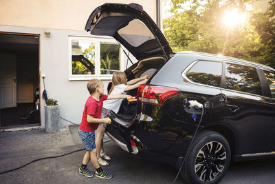 Kids loading black electric car trunk against house in back yard