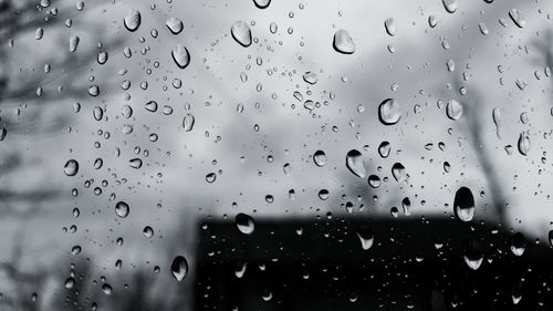 Close-up of water drops on glass against sky