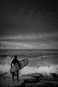 Man with surf looking at sea against sky