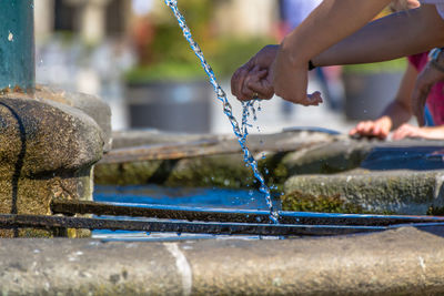 Cropped image of people washing hands in fountain on sunny summer day