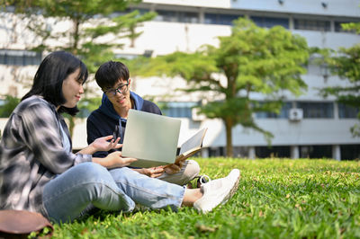 Friends using laptop while sitting on field