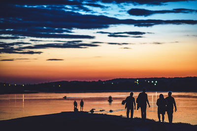 Silhouette people at beach against sky during sunset