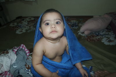 Cute baby girl wrapped in towel on bed at home