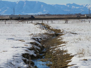 Stream on snow covered field against rocky mountains