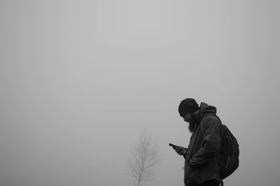 Man using mobile phone while standing against clear sky