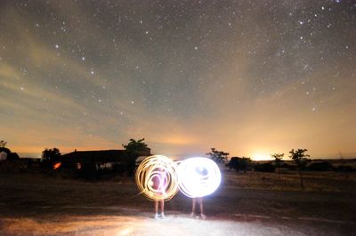 Illuminated lighting equipment on field against sky at night