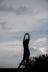 Silhouette woman with arms raised against sky during sunset