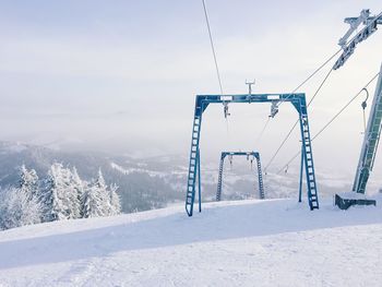 Ski lift over snow covered mountains against sky