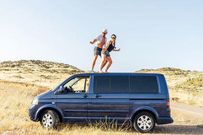 Happy couple surfing on top of the van.