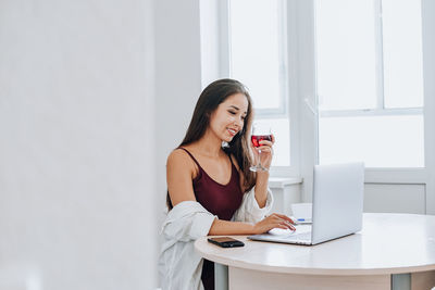 Young woman using phone while sitting on table