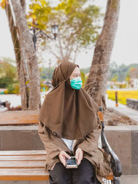 Woman wearing hijab and mask sitting on bench