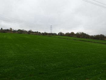 Electricity pylon on field against cloudy sky