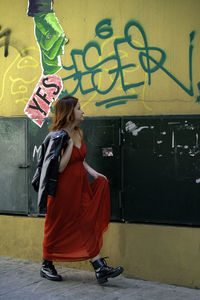 Side view of woman standing against graffiti wall