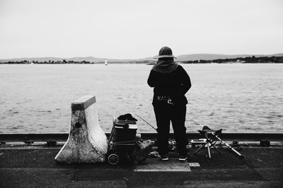 Rear view of man fishing on promenade against clear sky