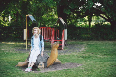 Full length of mid adult woman sitting on wooden tortoise statue in park