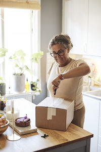 Woman with disability opening package using knife while standing in kitchen at home