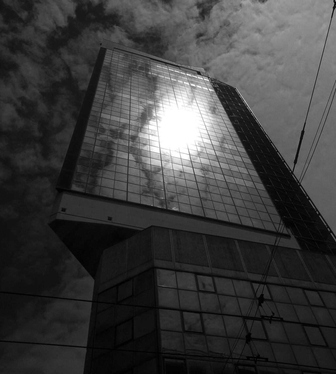 low angle view, architecture, built structure, building exterior, sky, sun, sunbeam, sunlight, cloud - sky, reflection, lens flare, building, glass - material, no people, day, outdoors, cloud, tower, modern, window