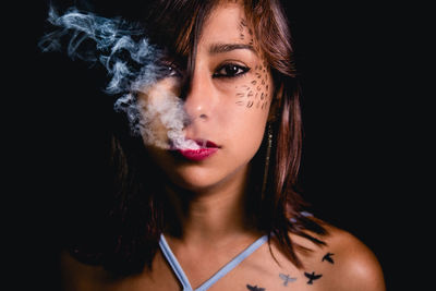 Portrait of young woman exhaling smoke against black background