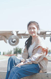 Portrait of smiling young woman sitting against sky