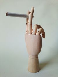 Close-up of wooden figurine holding cigarette against white background