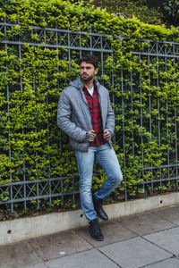 Full length of young man standing by railing against trees