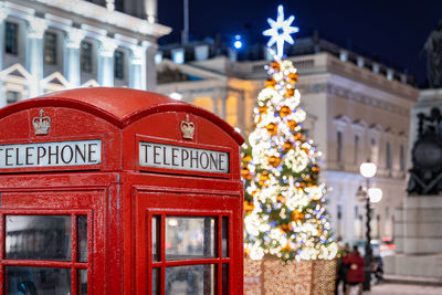 Red telephone booth against christmas tree in illuminated city